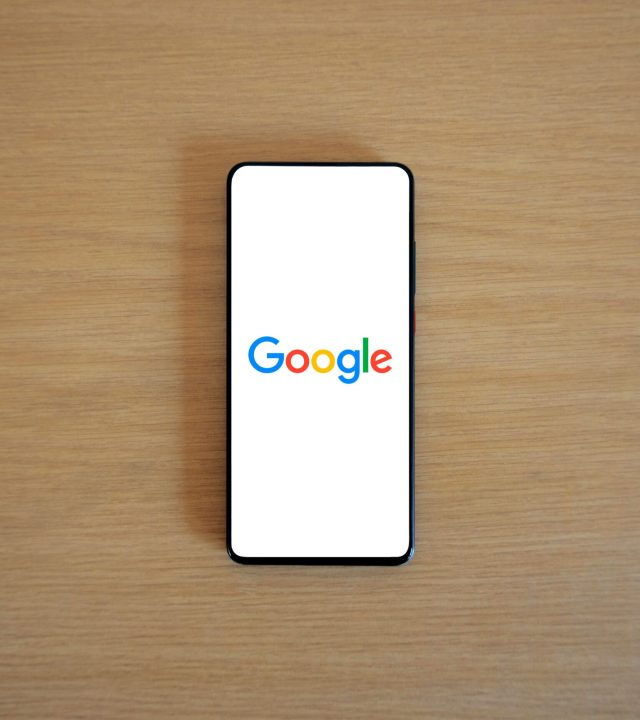 A smartphone displaying the Google homepage on a wooden surface, viewed from above.